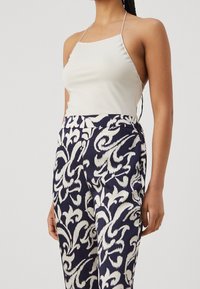 Vit ärmlös topp med tunna axelband, kombinerad med marinblå byxor med stort vitt blommönster. Slät tyg med modern passform.