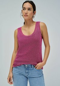 Fuksija pletena majica bez rukava s širokim izrezom i teksturiranim uzorkom, uparena s svijetloplavim trapericama. Srebrne kružne naušnice upotpunjuju izgled.