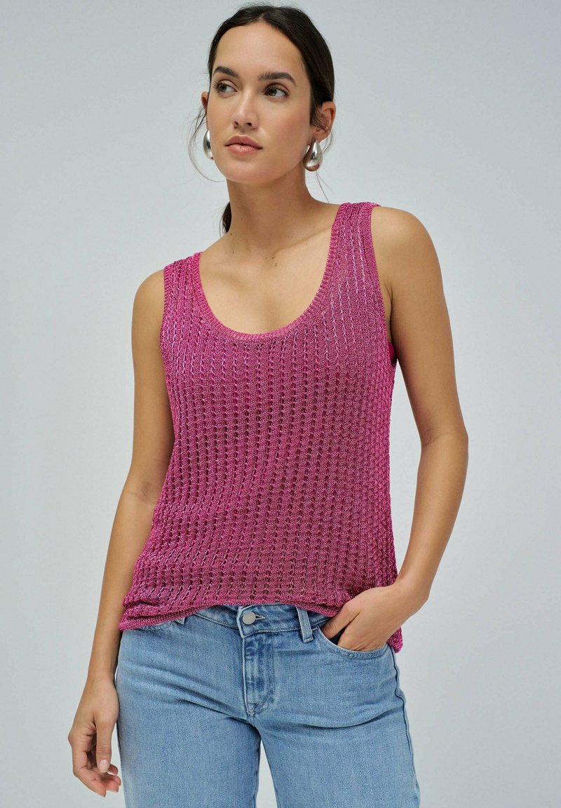 Fuksija pletena majica bez rukava s širokim izrezom i teksturiranim uzorkom, uparena s svijetloplavim trapericama. Srebrne kružne naušnice upotpunjuju izgled.