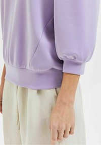 Sudadera de manga larga en color lavanda con una textura suave, que presenta mangas abullonadas y un dobladillo acanalado. Combinada con pantalones ligeros y holgados.