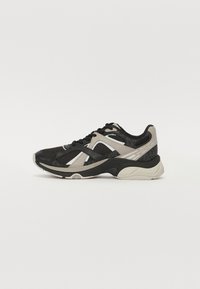 Sorte og beige sportsko med mesh-overdel, teksturerte detaljer og en polstret såle med gummigrep. Lisser i svart.