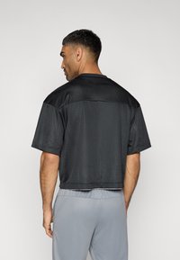 Μαύρο αθλητικό πουκάμισο από διχτυωτό ύφασμα με κοντά μανίκια, με άνετη γραμμή και υφή, συνδυασμένο με αθλητικό παντελόνι ανοιχτού γκρι χρώματος.