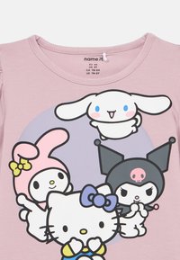 Jasnoróżowy bawełniany T-shirt z nadrukiem postaci z kreskówek, w tym Hello Kitty, na okrągłym fioletowym tle z zabawnymi wzorami.