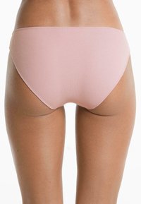 Nő ribbed világos rózsaszín bikini alsóruházatban, hátulról nézve, fehér háttér előtt.