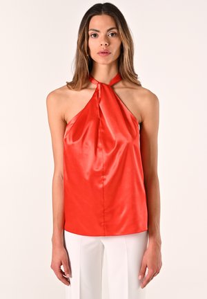 Top halter in raso rosso con scollatura annodata, caratterizzato da una texture uniforme e una vestibilità morbida, abbinato a pantaloni bianchi a gamba larga.