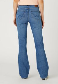 Blå denimflarejeans med medelhög midja, som har två bakfickor med en karakteristisk zigzag-stygn och minimal blekning.