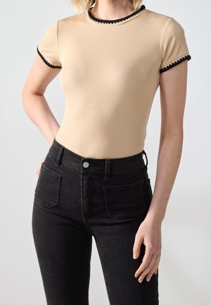 Haut beige à manches courtes côtelé avec bordure en crochet noire, porté avec un jean noir taille haute avec poches plaquées à l'avant.