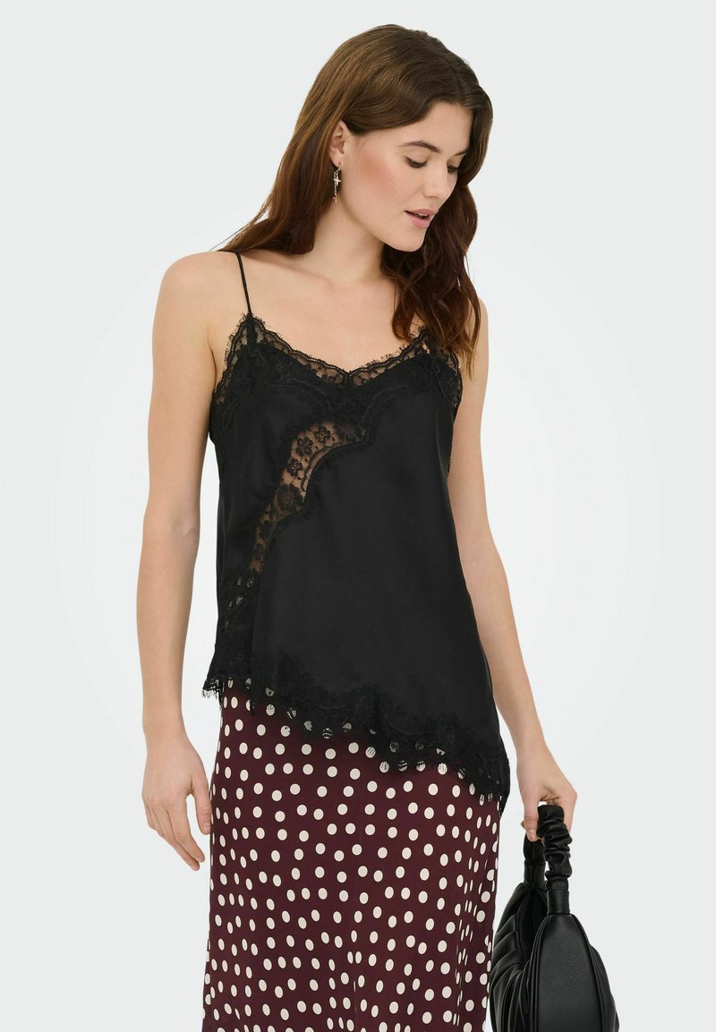 Czarny satynowy top na cienkich ramiączkach z koronkową lamówką i kwiatowymi wzorami, wyposażony w regulowane szelki i lekko rozkloszowany fason, zestawiony z spódnicą w grochy.