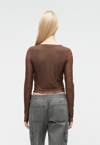 �Καφέ μακρυμάνικη μπλούζα με εφαρμοστή σχεδίαση και στρογγυλή λαιμόκοψη, συνδυασμένη με γκρι παντελόνι τύπου cargo με ελαστική μέση και πολλαπλές τσέπες.