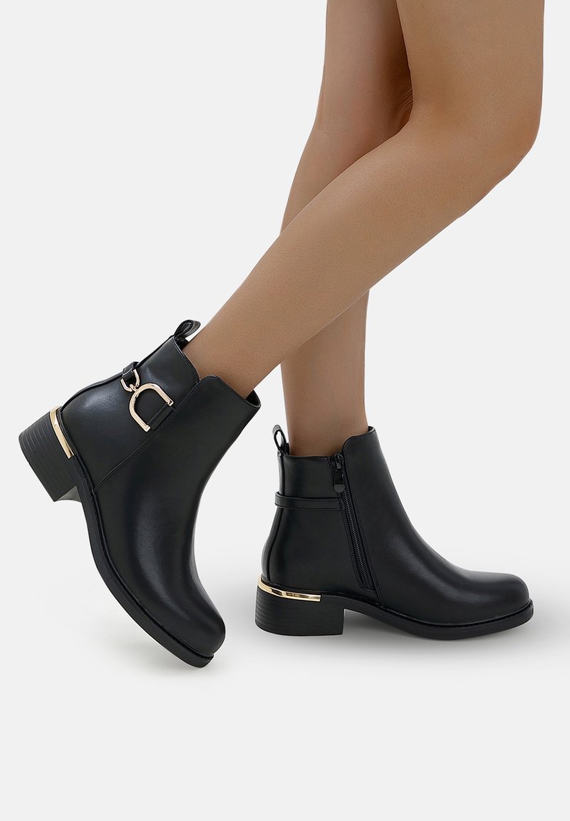 Bottines noires en cuir synthétique, avec un accent doré près du talon, une fermeture éclair sur le côté et un petit talon carré. Texture lisse.