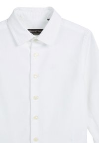 Witte katoen blouse met een kraag. Voorzien van zes knopen aan de voorkant en een ingebosseld logo op de borst. Hete fijne textuur.