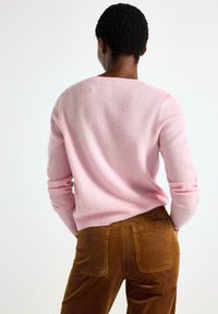 Lys lyserød, struktureret sweater med lange ærmer, rund hals og ribbede manchetter, parret med brune kordfløjlsbukser med baglommer.