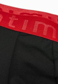 Černý elastický pás s červeným potiskem, s žebrovanou texturou. Tkanina je hladká a přizpůsobivá, vhodná pro aktivní nošení.