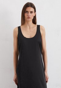 Robe noire sans manches avec encolure dégagée, texture lisse et coupe ample, descendant en dessous du genou, sans embellissements visibles.