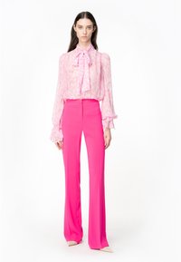 Roze blouse met een striknek en losse mouwen, gecombineerd met hooggeplaatste, wijde roze trousers. Glad materiaal met een subtiel patroon.