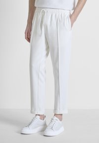 Witte joggingbroek van zachte stof, met een trekkoord in de taille, zijzakken en opgerolde boorden, gecombineerd met witte sneakers.