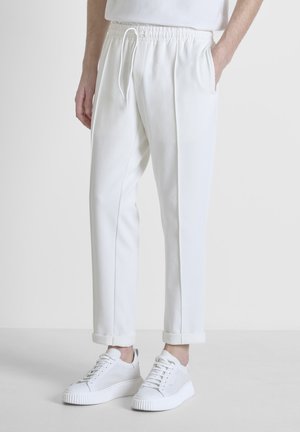 Witte joggingbroek van zachte stof, met een trekkoord in de taille, zijzakken en opgerolde boorden, gecombineerd met witte sneakers.