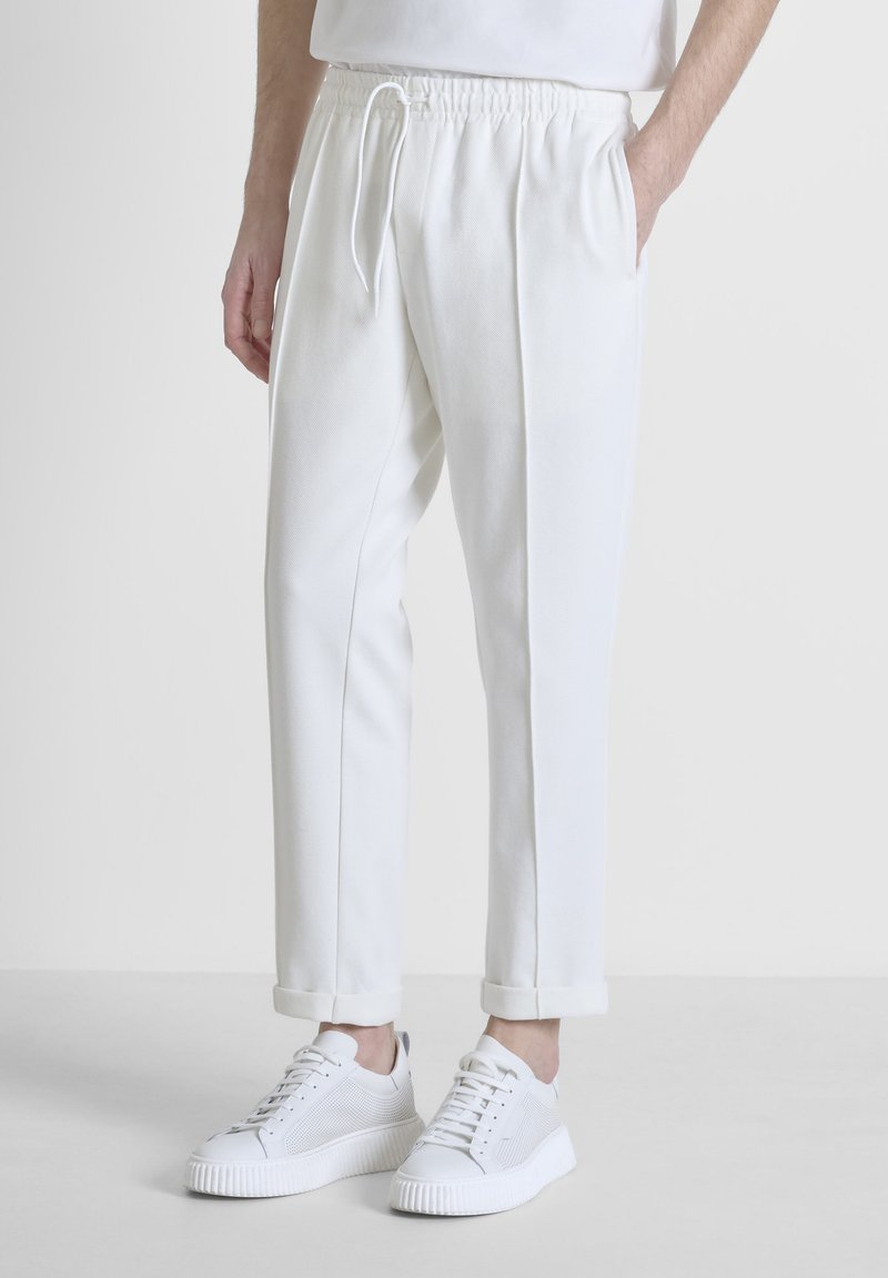 Witte joggingbroek van zachte stof, met een trekkoord in de taille, zijzakken en opgerolde boorden, gecombineerd met witte sneakers.