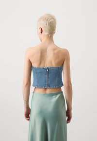 Denim stroppeløs topp med en tettsittende design, med glidelås bak. Kombinert med en silkeaktig grønn midikjole.