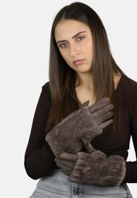 Guantes marrones con detalles de piel, que presentan una superficie texturizada, un diseño elegante y un agujero para el pulgar, usados por una persona con una camiseta negra.