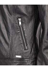 Schwarze Lederjacke mit einer Reißverschlusstasche und sichtbaren Nähten. Enthält ein metallisches Etikett nahe dem Saum und hat eine glatte Textur.