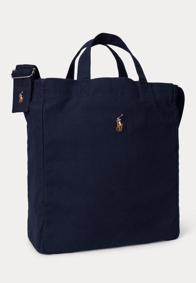 Τσάντα χειρός σε ναυτικό μπλε με κοντά χερούλια και ρυθμιζόμενο ιμάντα ώμου, διακοσμημένη με μικρά κεντημένα λογότυπα παίκτη πόλο στο μπροστινό μέρος και στον ιμάντα.