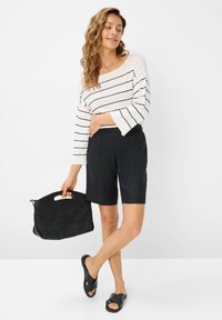 Maglietta a maniche lunghe bianca e nera a righe, pantaloni corti neri, sandali piatti neri e una borsa nera testurizzata con manico.