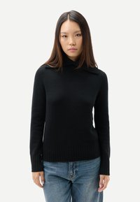 Svart tröja med hög krage, ribbad fåll och muddar. Tillverkad av mjukt tyg med en figurnära design och slät textur.