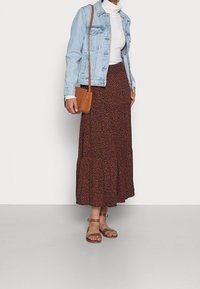 Veste en denim avec fermeture à boutons, col roulé blanc côtelé, jupe maxi à motifs bruns et sandales à talons couleur sable. Sac bandoulière marron inclus.