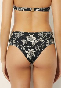 Chiloți negri de bikini cu un model floral alb, având frunze de palmier și frânghii. Design cu talie înaltă și textură de material neted.