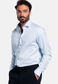 Lichtblauw overhemd met een slim fit, lange mouwen, button-down kraag en contrasterende gemusterde binnenkraag. Donkere broek gedragen.