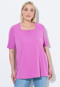 T-shirt di cotone viola con scollatura quadrata, maniche corte e vestibilità rilassata, abbinato a jeans in denim blu chiaro.