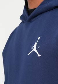 Hanorac de culoare albastru marin, realizat dintr-un material moale, care prezintă un logo Jumpman alb pe piept, cu o glugă confortabilă și manșete ribbate pentru un plus de confort.
