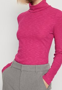 Tajt turtleneck i strukturerad, ribbad väv. Klarrosa färg. Långa ärmar. Kombinerad med grå höga byxor som visar detaljer för fickor.