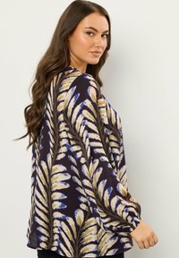 Blusa a maniche lunghe con una base viola scuro e motivo floreale crema. Presenta maniche a sbuffo e una vestibilità rilassata. Tessuto leggero.