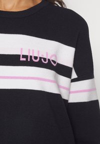 Pull en tricot noir avec des rayures horizontales blanches et roses, arborant le mot "LIU JO" en rose sur la poitrine.