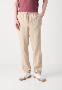 Beige, lette linbukser med elastisk midje og snøring. Teksturert overflate og løs passform for komfort. Kombinert med hvite joggesko.