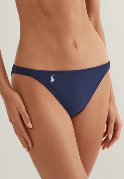 Slip de bikini bleu marin cu o textură netedă, având un mic logo alb în față și bretele laterale subțiri pentru o acoperire minimă.