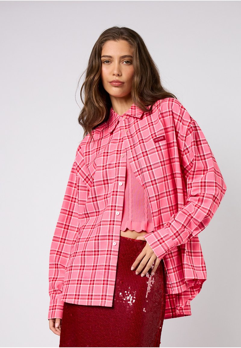 Różowa, oversize koszula w kratę z przodem na guziki, długimi rękawami i metką. Do tego różowy prążkowany crop top i czerwona spódnica z cekinami.