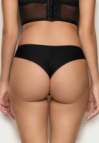 Ropa interior negra con una tela suave y elástica. Presenta un corte de bajo talle y una cobertura mínima en la parte trasera, con una cinturilla limpia.