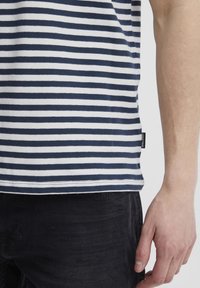 Navy and white striped t-shirt with a rounded hem, made of cotton. It has a small label on the side and is paired with dark jeans.