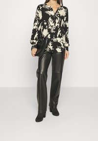 Blouse florale noire et crème à manches longues avec fermeture à boutons, associée à un pantalon moulant en cuir synthétique noir et des bottes noires à talons.
