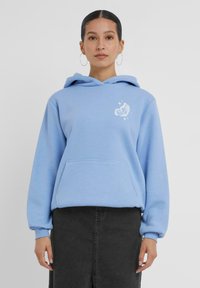 Felpa leggera blu, in misto cotone, con tasca frontale, cappuccio con cordini e grafica di una farfalla bianca sul petto. Gonna nera visibile sotto.