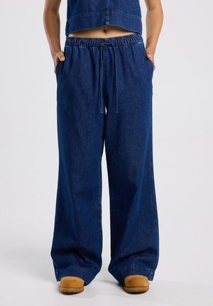 Wijdvallende blauwe spijkerbroek met een elastische tailleband en trekkoord. Beschikt over zijzakken en een relaxte pasvorm. Soepele textuur en stevige stof.