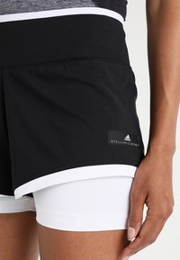 Black athletic shorts with a white trim, featuring a Stella McCartney label. Underneath, white fitted shorts are visible. Soft, stretchy fabric.