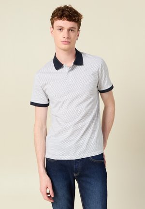 Camisa polo blanca con cuello y puños en navy, que presenta un sutil patrón geométrico. Textura suave, mangas cortas y un corte clásico.