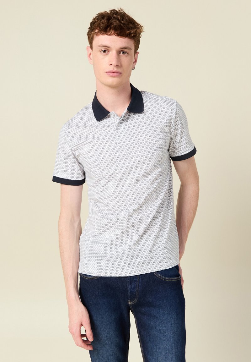 Camisa polo blanca con cuello y puños en navy, que presenta un sutil patrón geométrico. Textura suave, mangas cortas y un corte clásico.