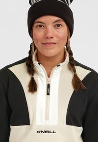 O'Neill fleece pullover met een kwart rits, voorzien van zwarte en crèmepanelen, een zachte textuur en een geborduurd logo aan de onderzijde.