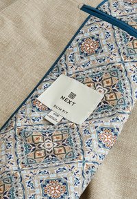 Bežna tkanina s teksturiranom završnom obradom, koja sadrži uzorčani deo u svijetloplavoj, narandžastoj i krem boji. Oznaka glasi "NEXT Slim Fit 40R."