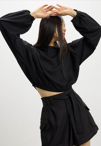 Felpa nera tagliata con orlo elasticizzato e maniche voluminose, abbinata a pantaloni corti neri sartoriali con cintura larga e tasche frontali.